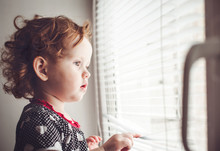 Little Girl Looking Out The Window Through The Blinds