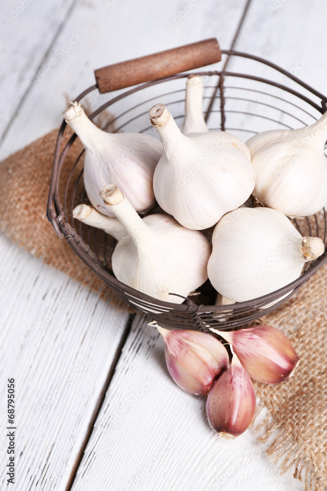 Fresh garlic in basket, on wooden background
