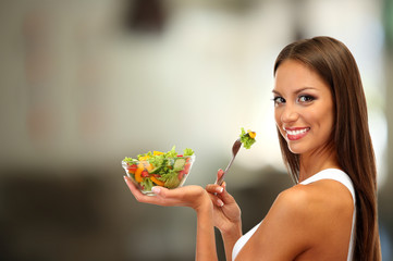 Beautiful young woman with salad on interior background