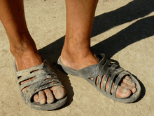 Dirty Male Feet In Rubber Slippers On Dried Earth