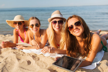 group of smiling young women with tablets on beach