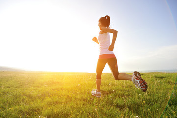 Wall Mural - Runner athlete legs running on sunrise grass seaside