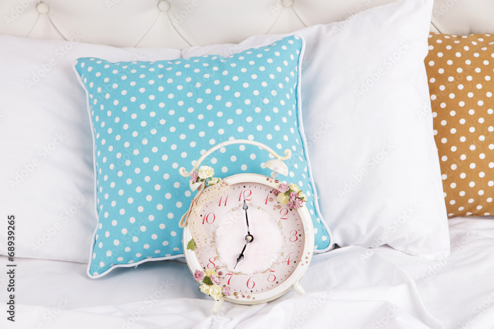 Metal clock on pillows on a big white bed