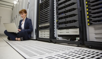 Wall Mural - Technician sitting on floor beside server tower using laptop