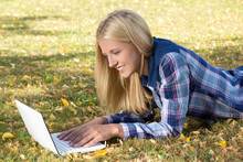 Beautiful Woman Lying In Autumn Park And Using Laptop