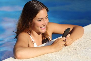 Girl using a smart phone in a pool in summer vacations