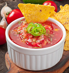 Mexican nacho chips and salsa dip in bowl on wooden background