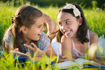 Two happy child girls studying on grass