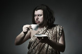 Fototapeta  - Savage man in skin of beast drink tea or coffee