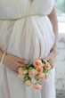 Closeup on tummy of pregnant woman, wearing long white dress, ho