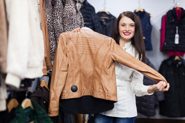 Wall Mural - Cute young woman choosing jacket at clothing store