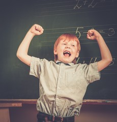 Fototapete - Little funny redhead schoolboy near blackboard