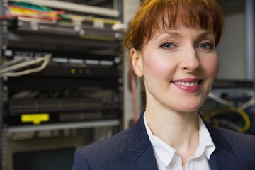 Pretty technician smiling at camera beside open server