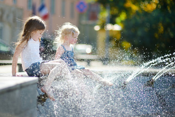 Two cute little girls playing with a city fountain