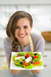 Portrait of smiling young housewife showing greek salad