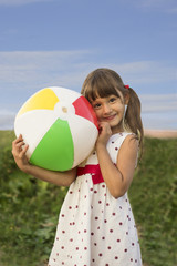 Happy smiling little girl playing with ball outdoors in summer