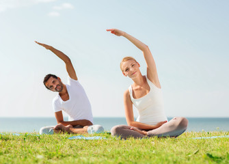 Canvas Print - smiling couple making yoga exercises outdoors