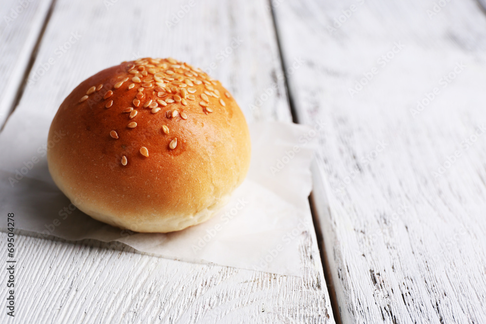 Tasty bun with sesame on color wooden background