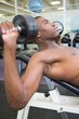 © WavebreakMediaMicro - Shirtless young man exercising with dumbbells in gym