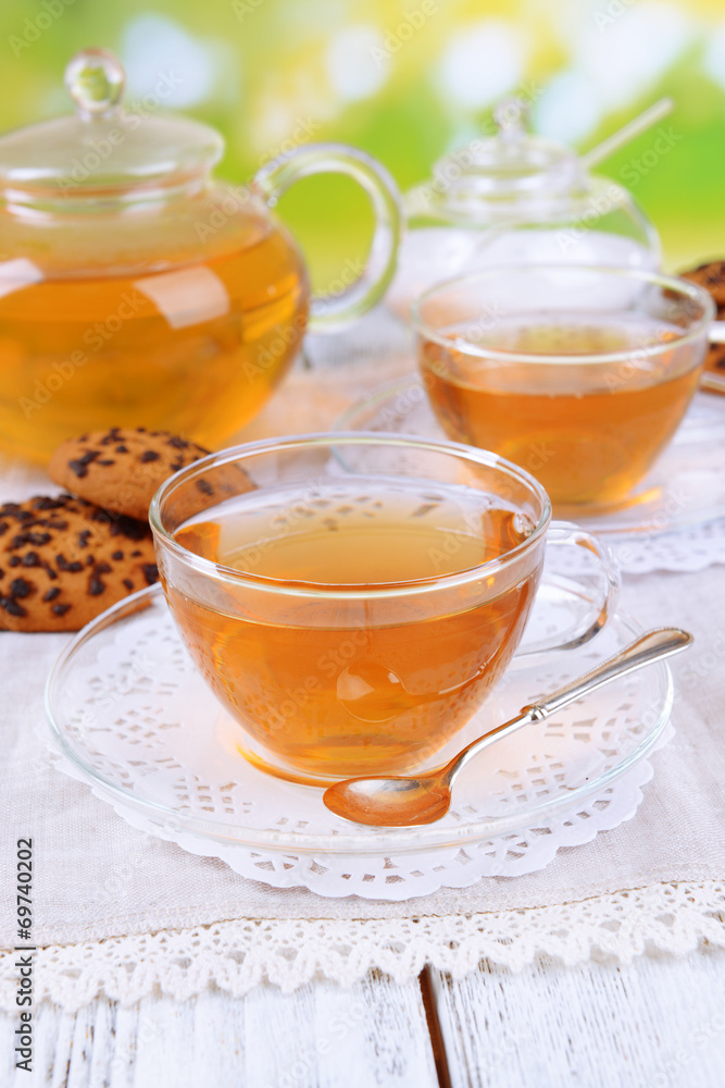 Teapot and cups of tea on table on bright background