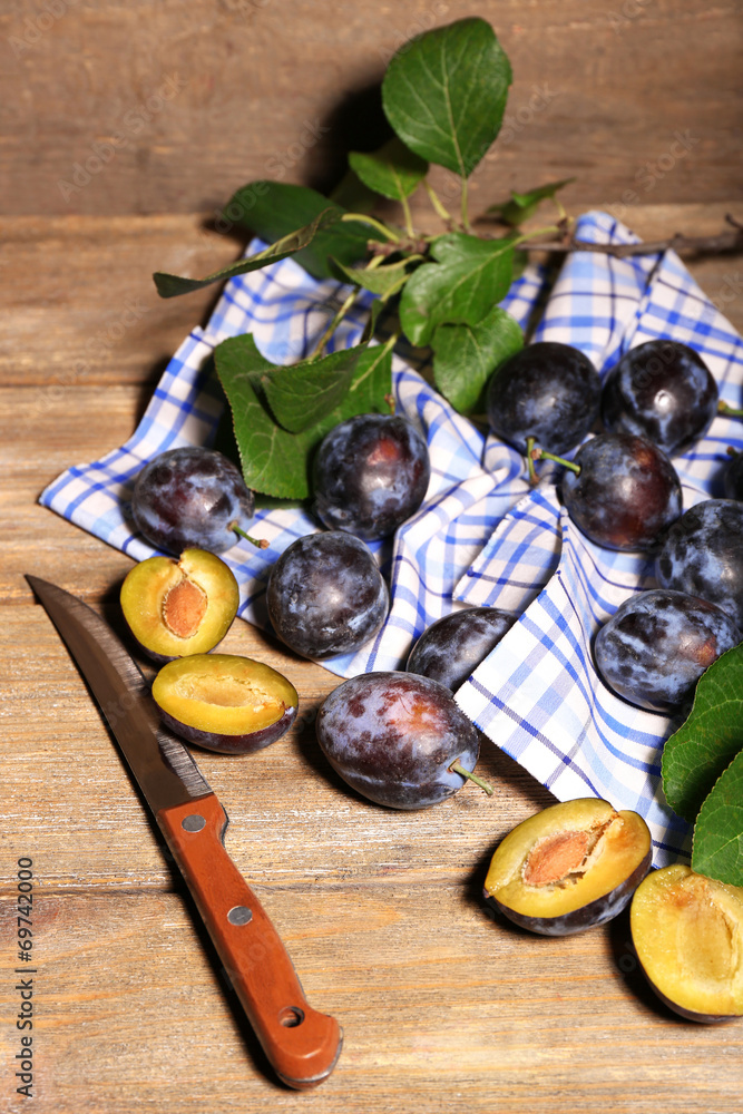 Ripe sweet plums with leaves, on wooden table