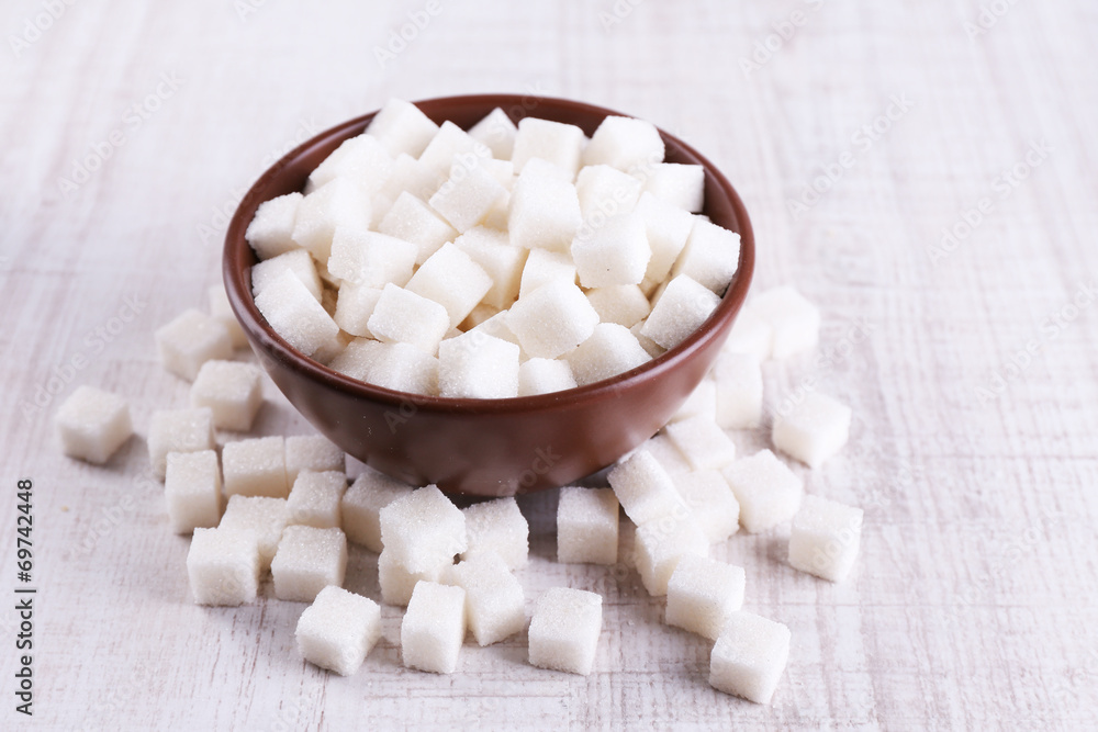 Refined sugar in color bowl on wooden background