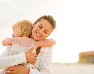 Wall Mural - Portrait of mother and baby girl hugging on the beach 