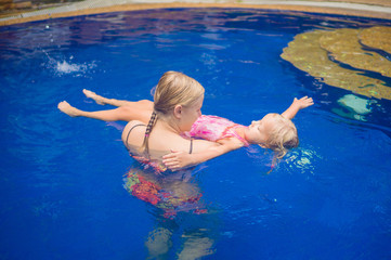 Young mother and adorable daughter having fun in pool. Learning