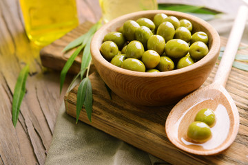 Green olives in bowl with leaves on table close-up