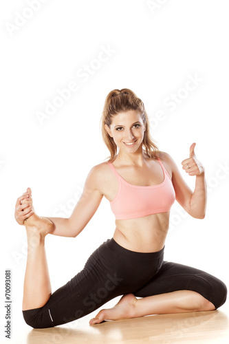 Plakat uśmiechnięta młoda dziewczyna robi ćwiczenia jogi i pokazując kciuk do góry