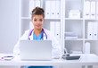 © lenets_tan - Female doctor sitting on the desk and working a laptop in hospi