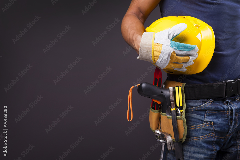 Close up of a worker with toolbelt and helmet against black back - obrazy, fototapety, plakaty 