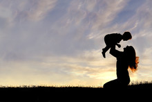 Silhouette Of Happy Mother Playing Outside With Baby