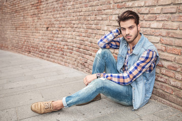 Poster - handsome man resting on the sidewalk, leaning against a wall