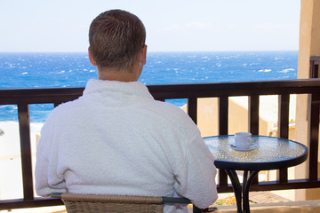 back view of man sitting on balcony with sea view