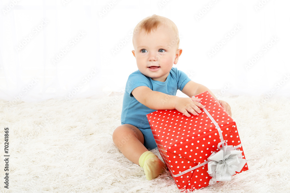 Cute baby boy with present box on carpet in room