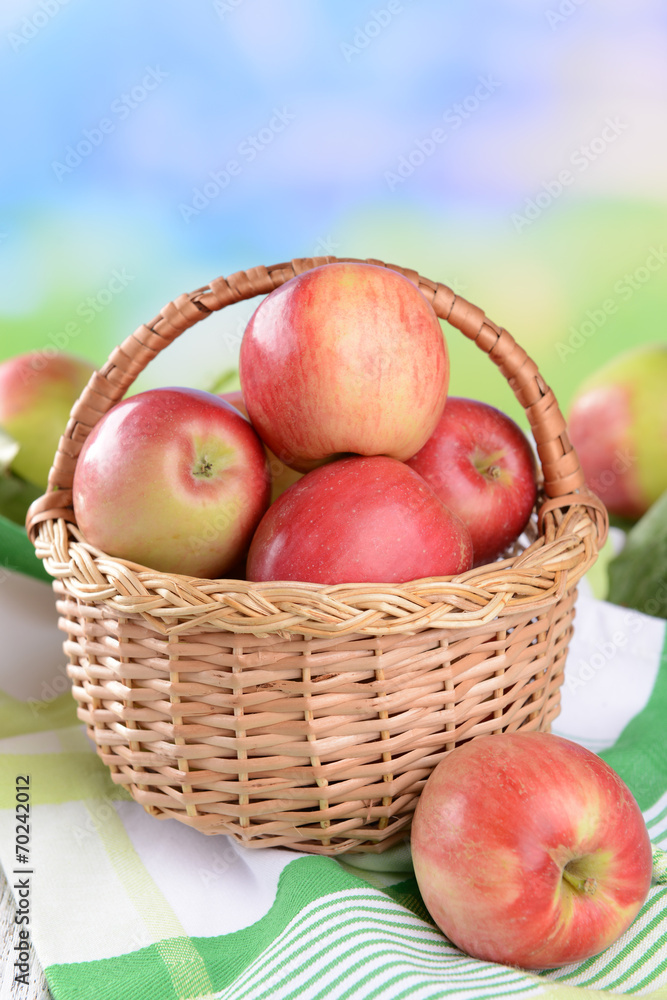 Sweet apples in wicker basket on table on bright background