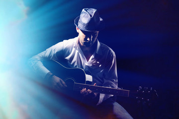 Canvas Print - Young musician playing acoustic guitar, on dark background