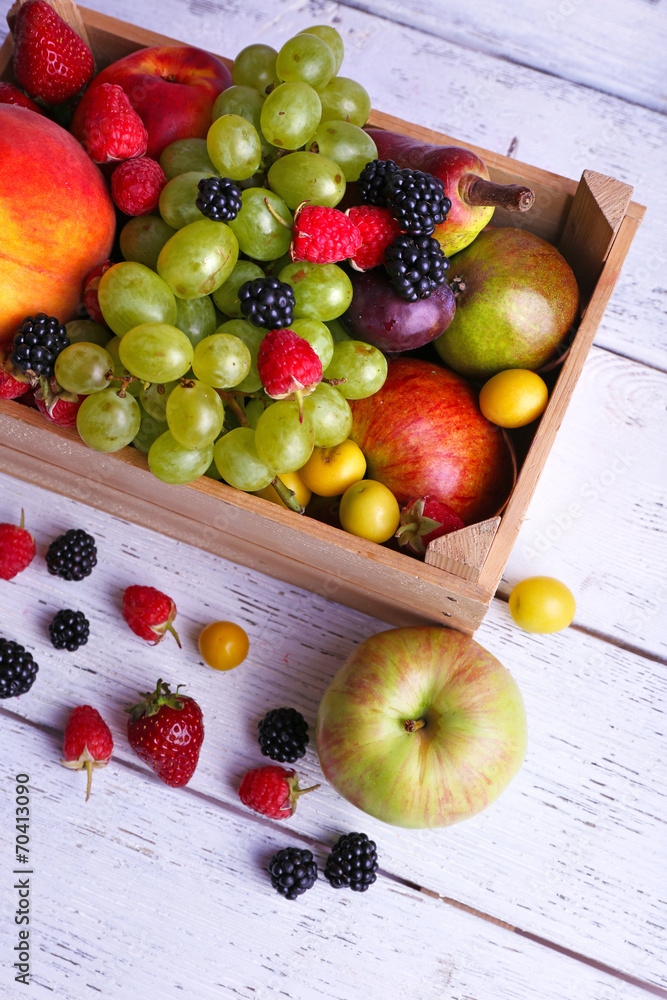 Different berries and fruits in box on wooden table close-up