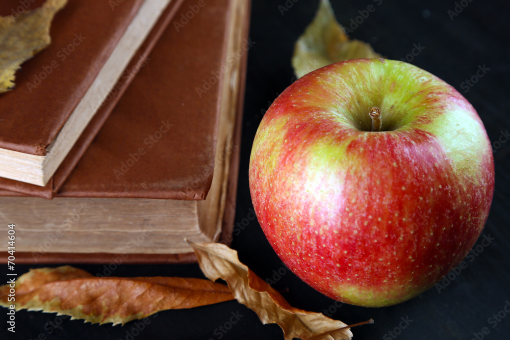 Apple with books and dry leaves on wooden background
