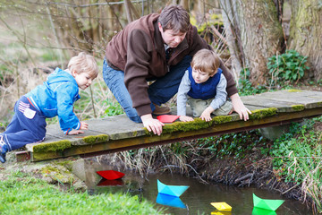 Wall Mural - Two little brothers and their dad playing with paper boats by a