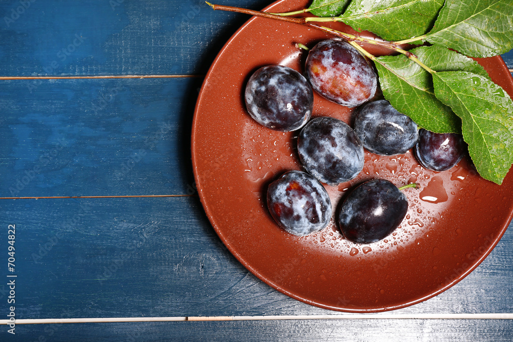 Ripe sweet plums on brown plate, on wooden table