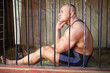 Sad strongman sits with his head by hand in the cage for animals