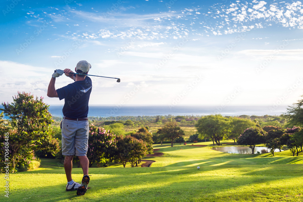 Man hitting golf ball down hill towards ocean and horizon - obrazy, fototapety, plakaty 