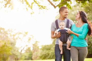 Family With Baby Son In Carrier Walking Through Park