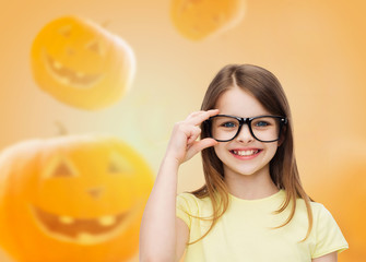 Wall Mural - smiling girl in glasses over pumpkins background