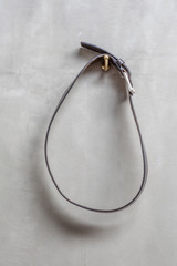 The loop of black leather belt is hanging on exposed concrete w