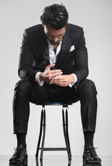 man in tuxedo looking down while sitting on a stool,