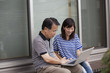 © Mint Images - A man and a women sitting outside a house. Holding a laptop computer.