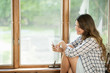 © Mint Images - A woman sitting by a window, looking at her cell phone.